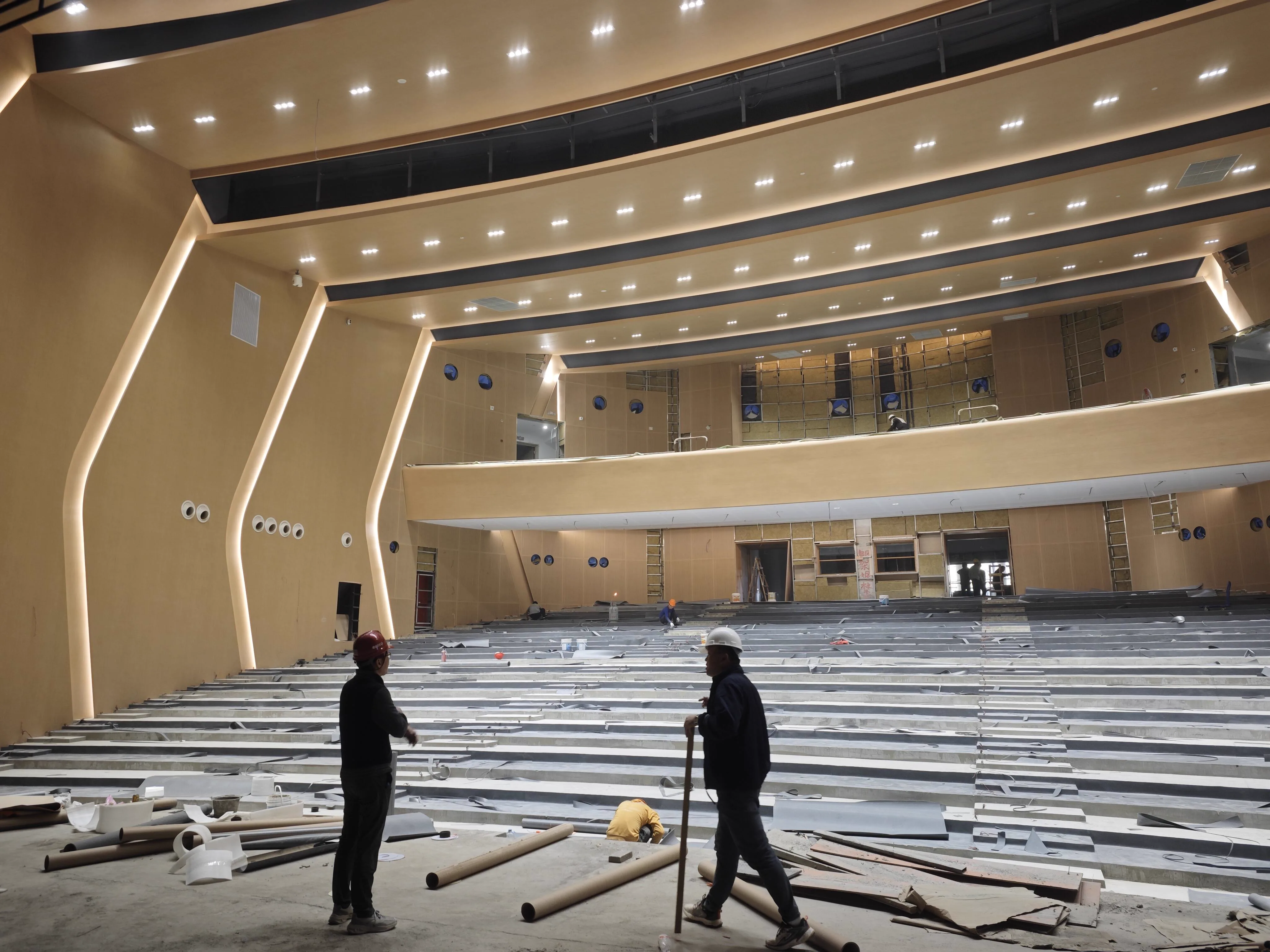Auditorium construction phase with tiered seating base framework and workers in the audience area